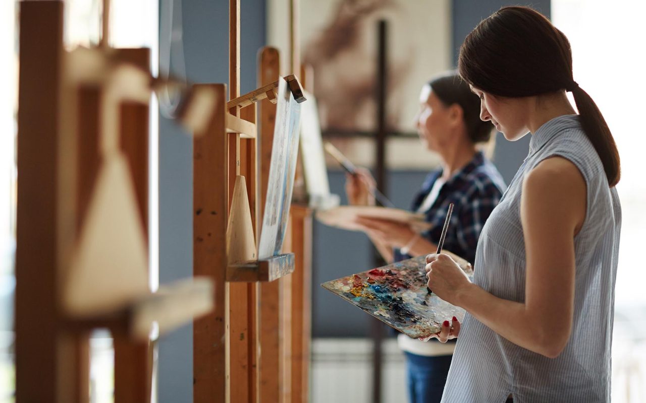 Side view portrait of young female student in art class, painting oil picture on canvas