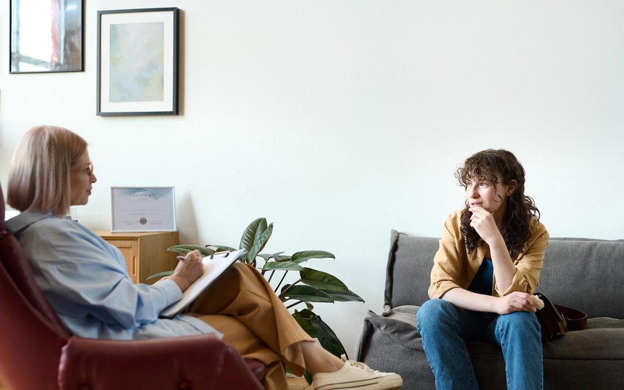 Young woman sitting on sofa and having psycho session with therapist in office
